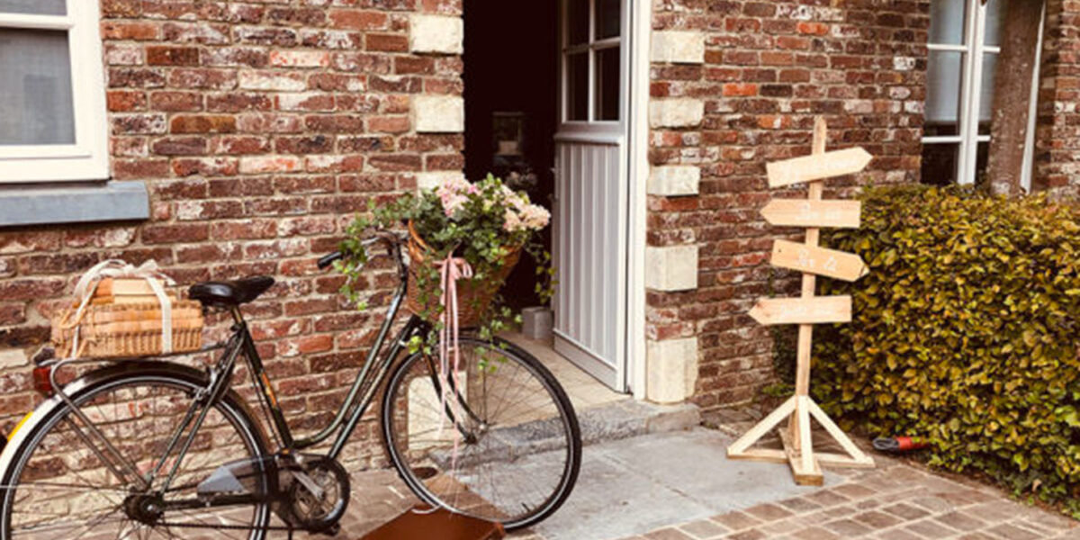 Vélo avec une valise ancienne et un panneau indiquant des directions à l'Hôtel Koru dans le Brabant-Wallon