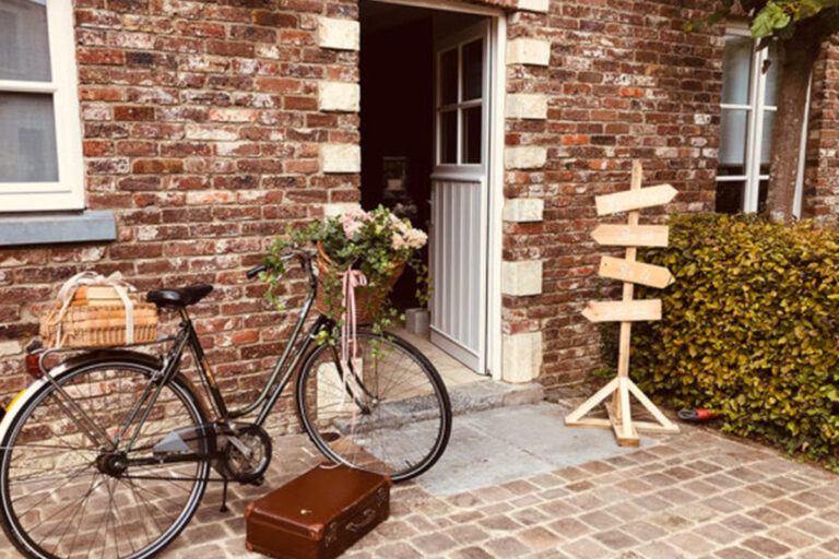 Vélo avec une valise ancienne et un panneau indiquant des directions à l'Hôtel Koru dans le Brabant-Wallon